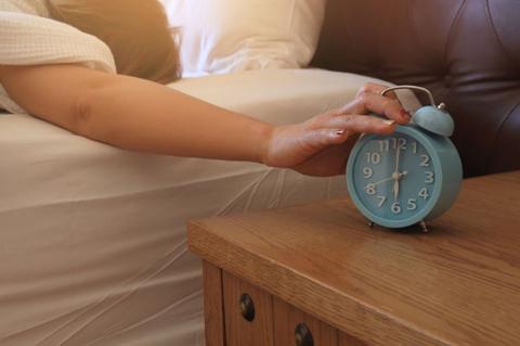 Close up of woman hand in bedroom trying to wake up with alarm clock feeling Exhausted and overworked working in the night on the bed; Shutterstock ID 1604315812; purchase_order: aljazeera ; job: ; client: ; other: